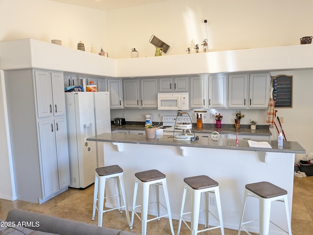 11424 S Obispo Dr, Goodyear, AZ 85338 - kitchen featuring white appliances, a kitchen breakfast bar, gray cabinets, light tile patterned floors, and dark stone countertops