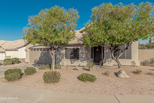 view of property hidden behind natural elements featuring a garage, driveway, a tiled roof, and stucco siding