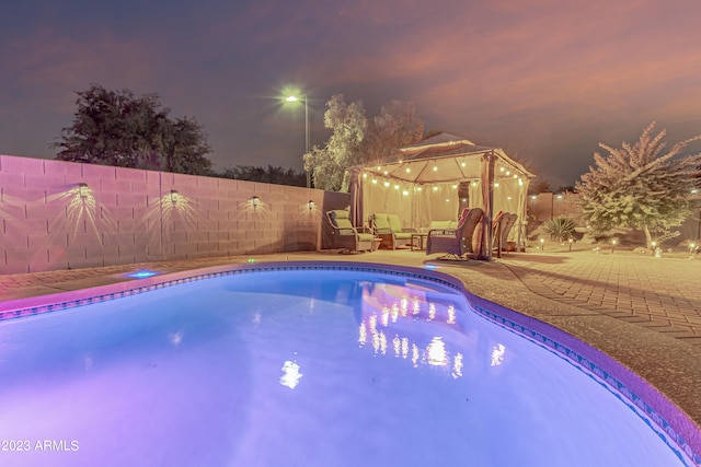 pool at twilight featuring a fenced in pool, outdoor lounge area, a gazebo, a patio area, and a fenced backyard