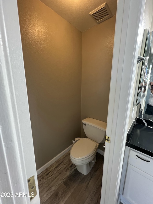 bathroom with baseboards, visible vents, toilet, and wood finished floors