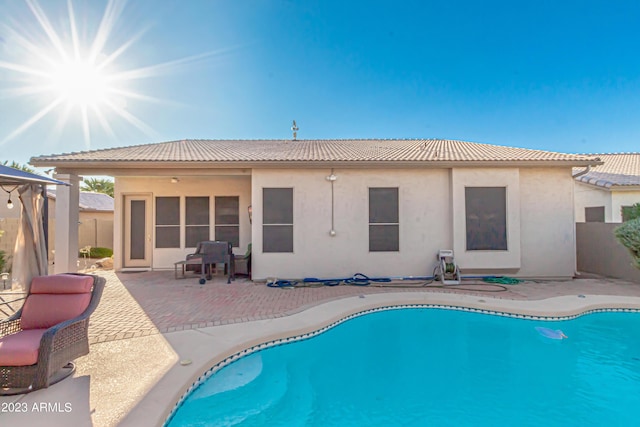 rear view of house with an outdoor pool, a patio, a tiled roof, fence, and stucco siding