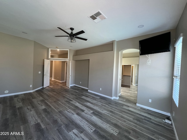 unfurnished bedroom with dark wood-type flooring, arched walkways, visible vents, and baseboards