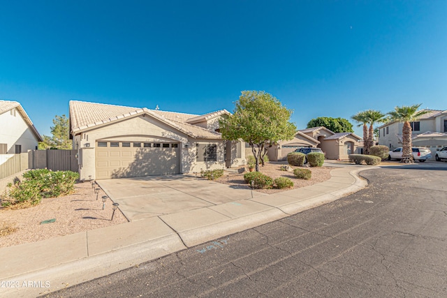 view of front facade with an attached garage, a tile roof, fence, driveway, and stucco siding