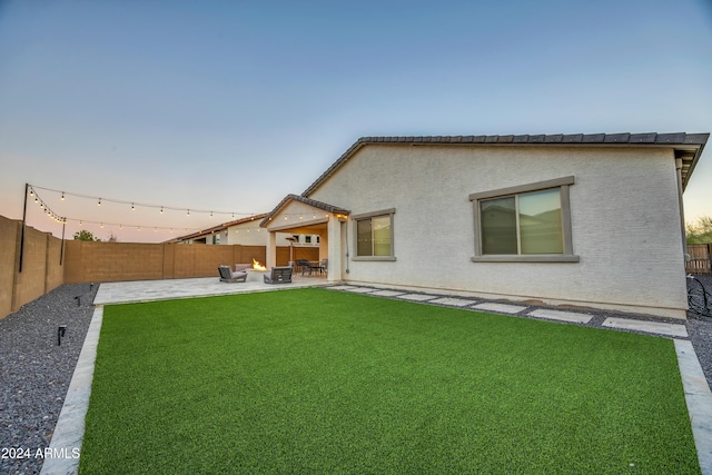 back house at dusk featuring a patio area and a lawn