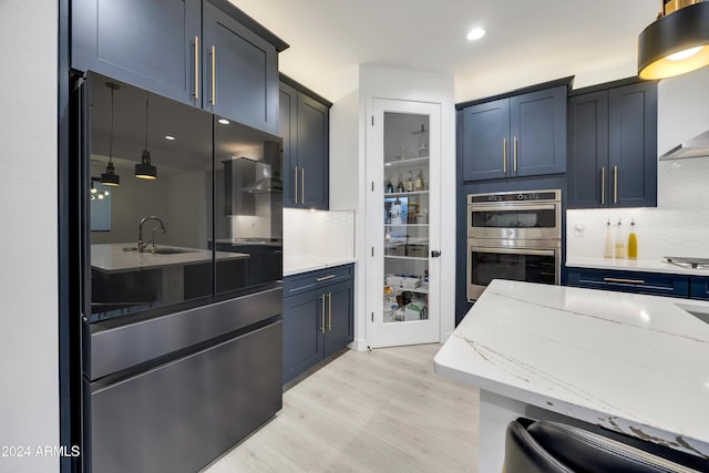 kitchen with light stone countertops, appliances with stainless steel finishes, backsplash, blue cabinets, and light hardwood / wood-style flooring