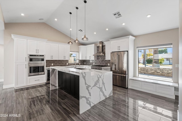 kitchen with plenty of natural light, wall chimney range hood, an island with sink, and appliances with stainless steel finishes