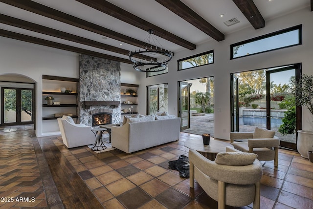 living room featuring french doors, built in shelves, beam ceiling, a fireplace, and a high ceiling