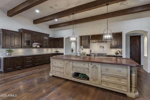 kitchen with wall chimney range hood, butcher block counters, and a center island with sink