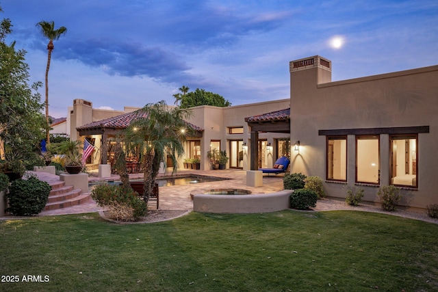 back house at dusk with a yard and a patio