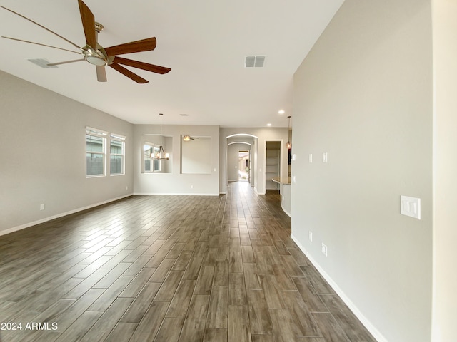 unfurnished living room featuring ceiling fan with notable chandelier and dark hardwood / wood-style flooring