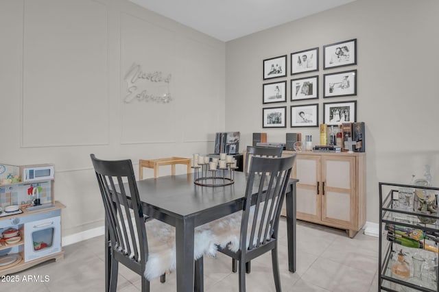 dining space featuring baseboards, a decorative wall, and light tile patterned flooring