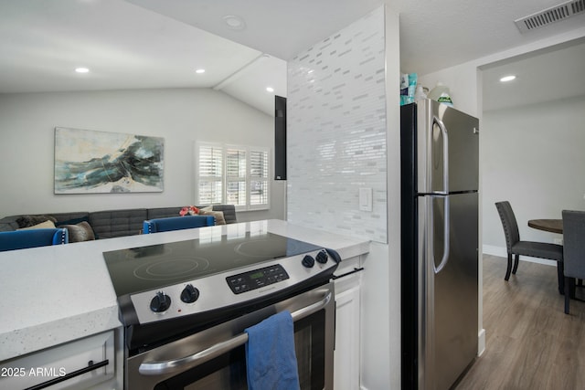 kitchen with lofted ceiling, backsplash, wood-type flooring, white cabinetry, and stainless steel appliances