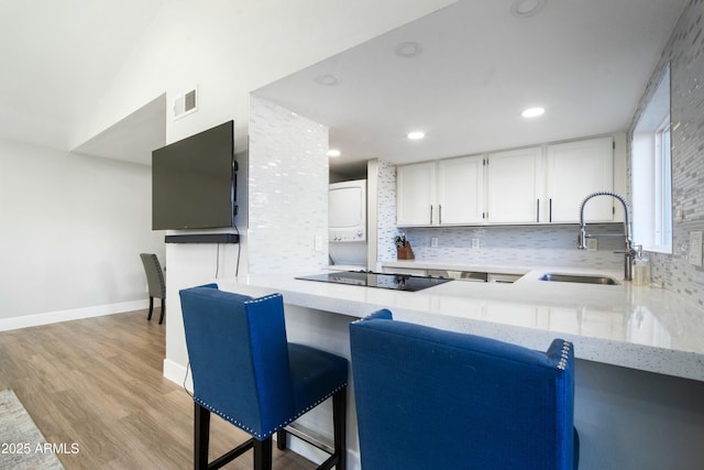 kitchen with tasteful backsplash, kitchen peninsula, sink, white cabinetry, and black electric cooktop