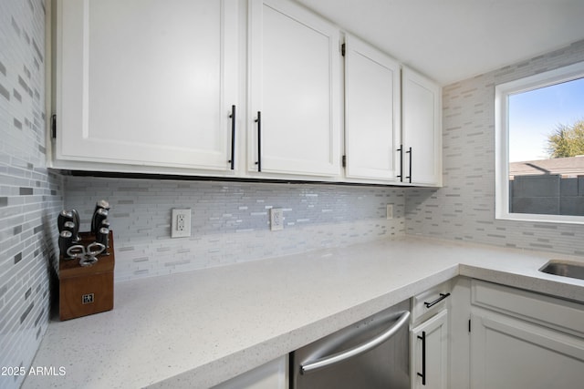 kitchen featuring stainless steel dishwasher, decorative backsplash, sink, light stone countertops, and white cabinets