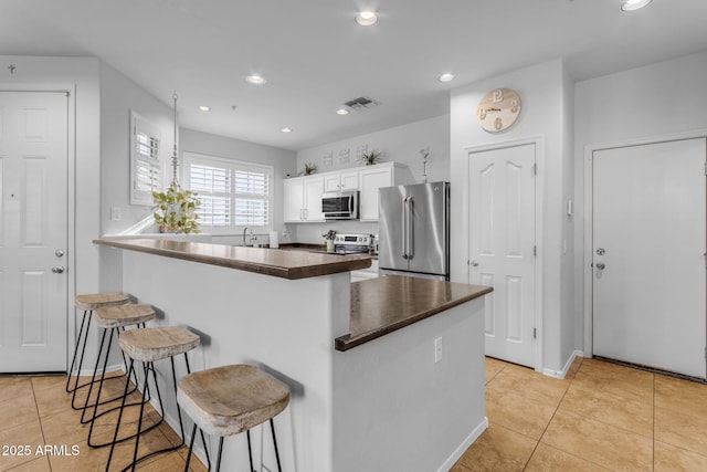 kitchen featuring a kitchen bar, white cabinetry, light tile patterned floors, kitchen peninsula, and stainless steel appliances