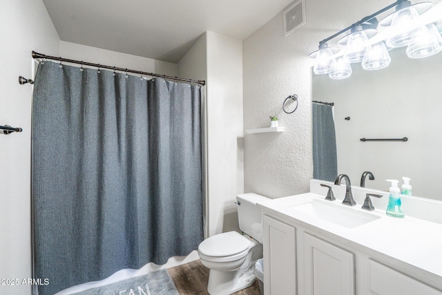 bathroom featuring visible vents, a textured wall, toilet, wood finished floors, and vanity