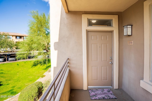 property entrance featuring a balcony, a lawn, and stucco siding