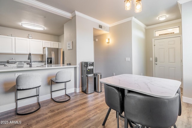 kitchen featuring a kitchen breakfast bar, white cabinetry, light wood finished floors, and stainless steel fridge with ice dispenser