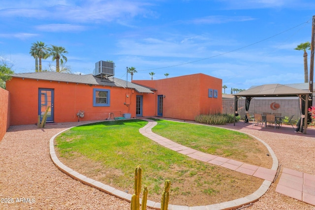 rear view of property featuring fence, central AC, stucco siding, a gazebo, and a patio area