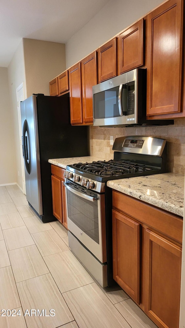 3347 W Steinbeck Dr, Anthem, AZ 85086 - kitchen with appliances with stainless steel finishes, brown cabinets, tasteful backsplash, and light stone countertops