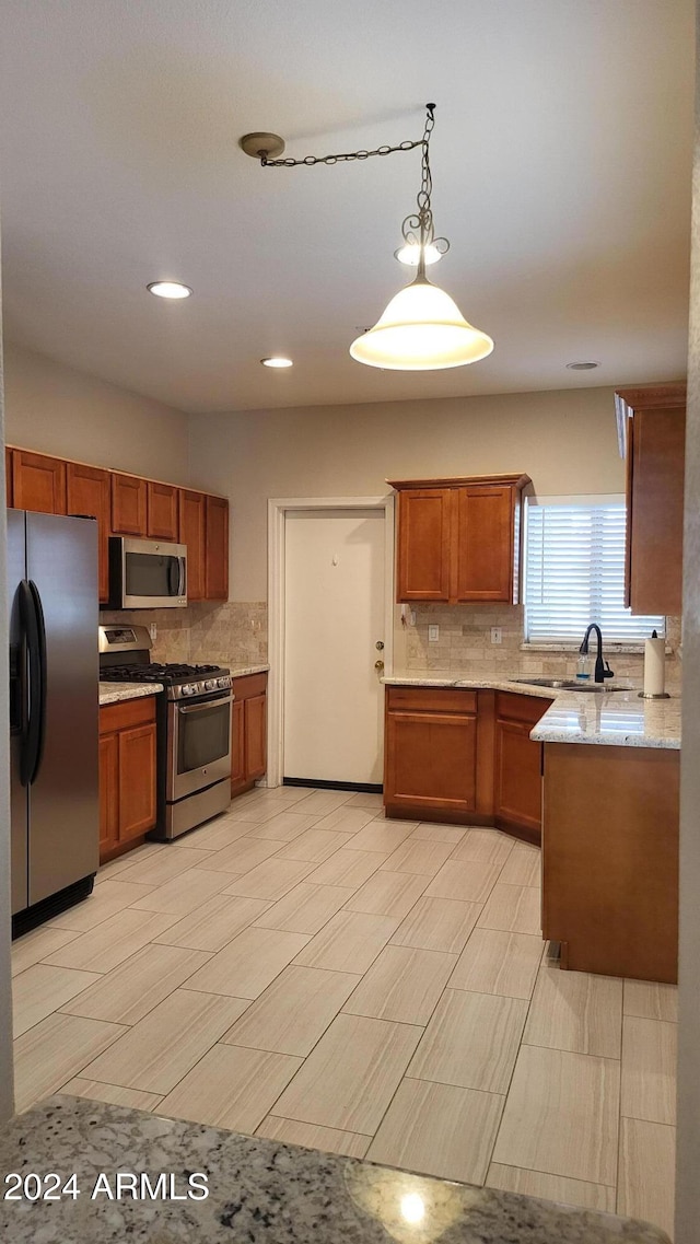 kitchen with tasteful backsplash, hanging light fixtures, stainless steel appliances, sink, and light stone counters