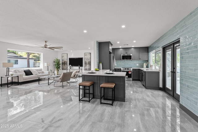 kitchen featuring gray cabinets, light countertops, appliances with stainless steel finishes, a kitchen bar, and open floor plan