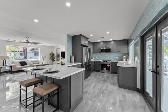 kitchen with a peninsula, light countertops, gray cabinets, and stainless steel appliances