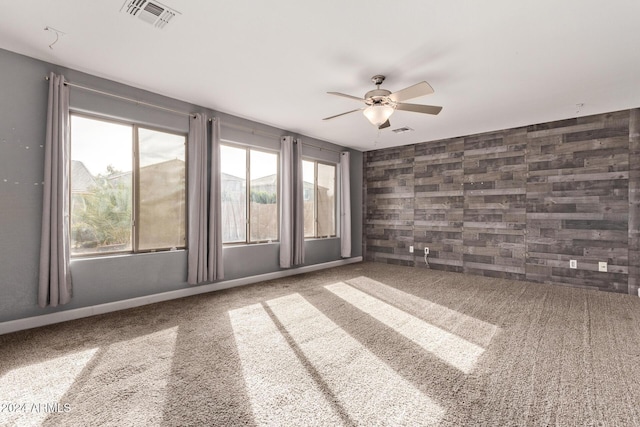 carpeted spare room with ceiling fan and wooden walls