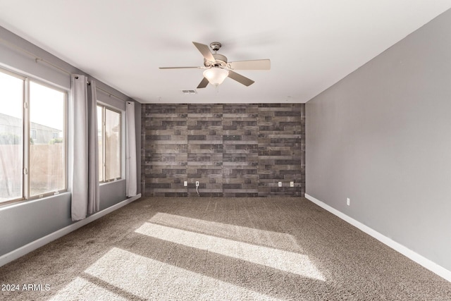 empty room featuring carpet, ceiling fan, and wooden walls