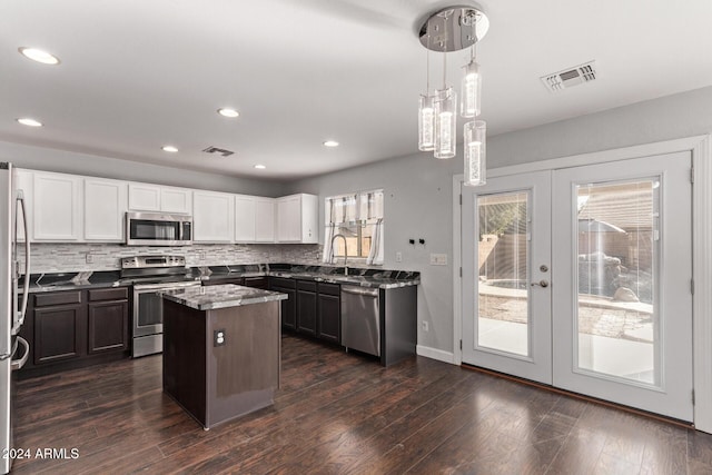 kitchen with light stone countertops, french doors, decorative light fixtures, a kitchen island, and appliances with stainless steel finishes