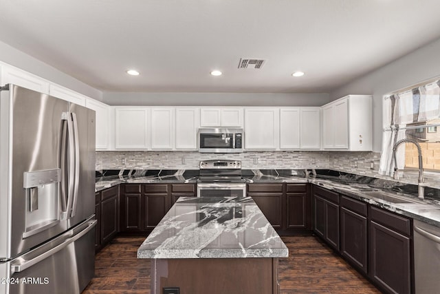 kitchen featuring appliances with stainless steel finishes, light stone counters, dark wood-type flooring, sink, and a kitchen island