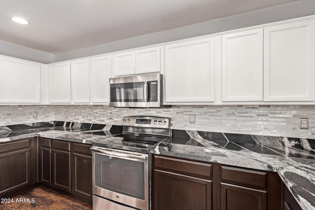 kitchen with appliances with stainless steel finishes, backsplash, dark wood-type flooring, dark stone countertops, and white cabinetry