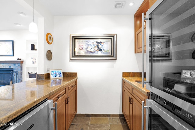 kitchen featuring brown cabinetry, visible vents, a fireplace, and stone countertops