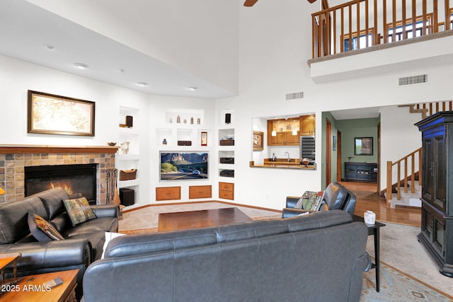 carpeted living area with built in features, visible vents, a glass covered fireplace, and stairs