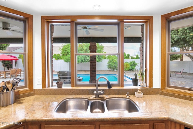 kitchen with a sink, light stone countertops, and ceiling fan