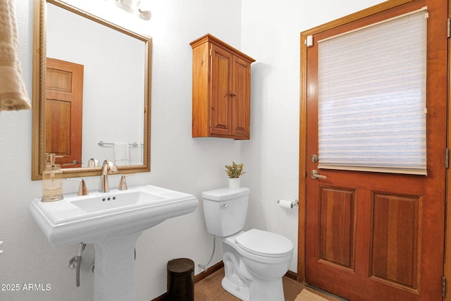 half bath featuring tile patterned floors, toilet, baseboards, and a sink