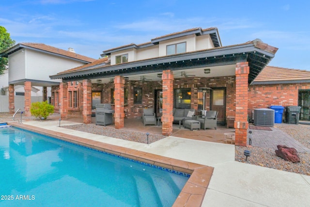 rear view of property with a patio, outdoor lounge area, an outdoor pool, brick siding, and central AC unit