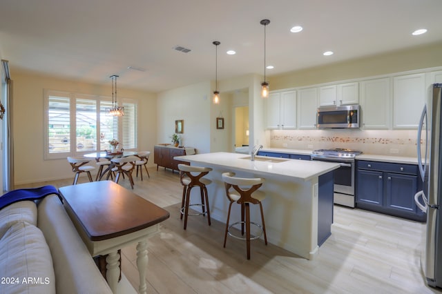 kitchen featuring hanging light fixtures, white cabinetry, appliances with stainless steel finishes, a center island with sink, and tasteful backsplash