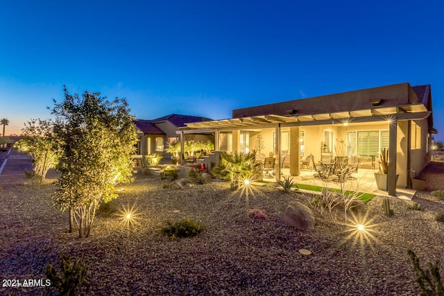 back house at dusk featuring a patio and a pergola