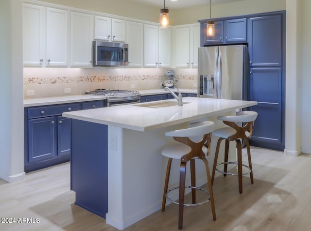 kitchen with hanging light fixtures, stainless steel appliances, a center island with sink, tasteful backsplash, and blue cabinets