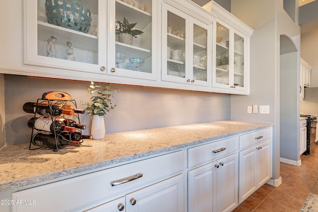 bar with white cabinets, black stove, light stone countertops, and light tile patterned flooring