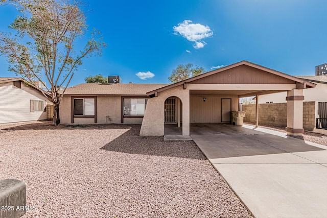 ranch-style home with central air condition unit, an attached carport, concrete driveway, and stucco siding