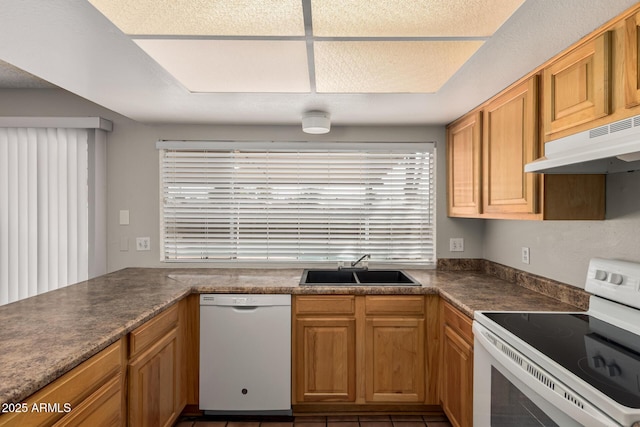 kitchen featuring white appliances, dark countertops, under cabinet range hood, and a sink