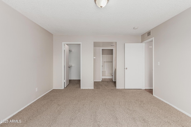 unfurnished bedroom featuring a spacious closet, visible vents, baseboards, carpet, and a textured ceiling