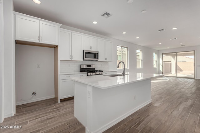 kitchen featuring appliances with stainless steel finishes, white cabinetry, and an island with sink