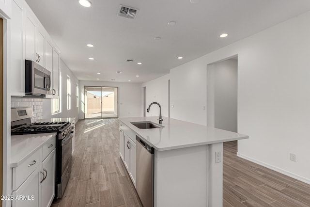 kitchen with appliances with stainless steel finishes, light wood-type flooring, a kitchen island with sink, sink, and white cabinets