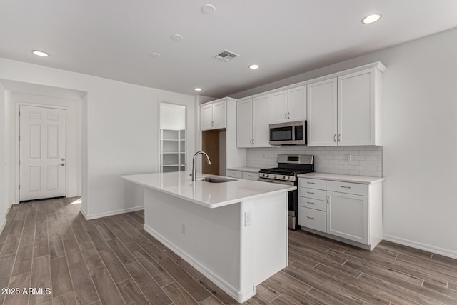 kitchen with sink, an island with sink, appliances with stainless steel finishes, tasteful backsplash, and white cabinetry