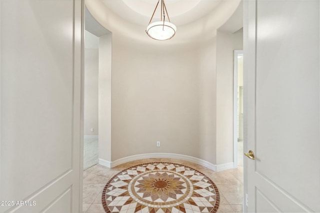 hall featuring light tile patterned floors, baseboards, and a tray ceiling