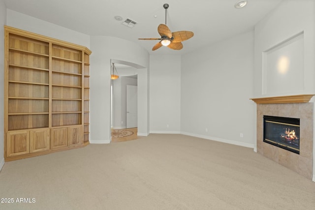 unfurnished living room with baseboards, visible vents, a ceiling fan, a tiled fireplace, and carpet flooring