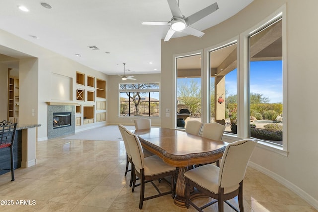 dining space featuring baseboards, visible vents, a ceiling fan, built in features, and a glass covered fireplace